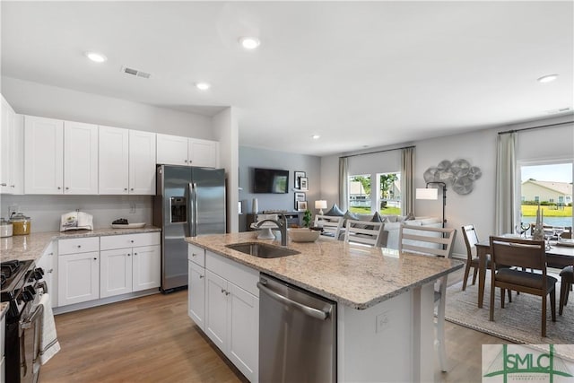 kitchen featuring stainless steel appliances, a sink, light stone counters, white cabinetry, and recessed lighting