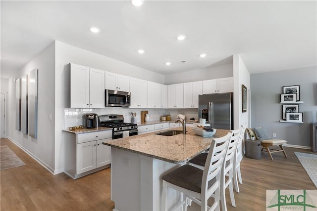 kitchen featuring stainless steel appliances, a sink, a kitchen bar, light stone counters, and baseboards