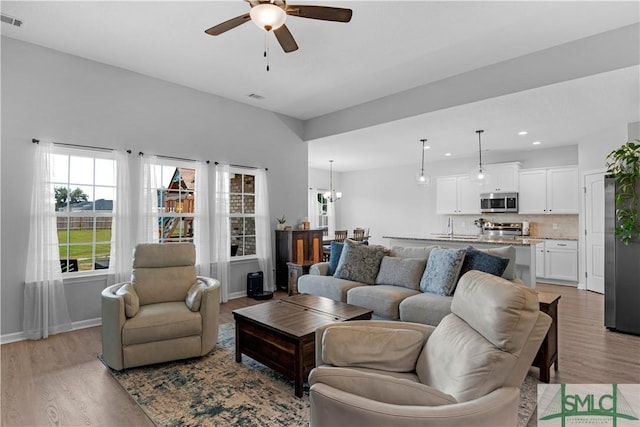 living room featuring ceiling fan, light wood-style floors, recessed lighting, baseboards, and a chandelier