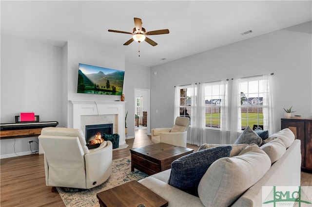 living area featuring wood finished floors, ceiling fan, a fireplace with flush hearth, and healthy amount of natural light