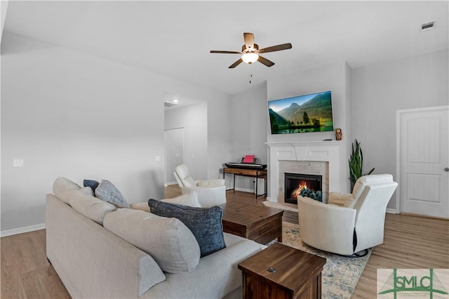 living room with a ceiling fan, light wood finished floors, a fireplace with flush hearth, and baseboards
