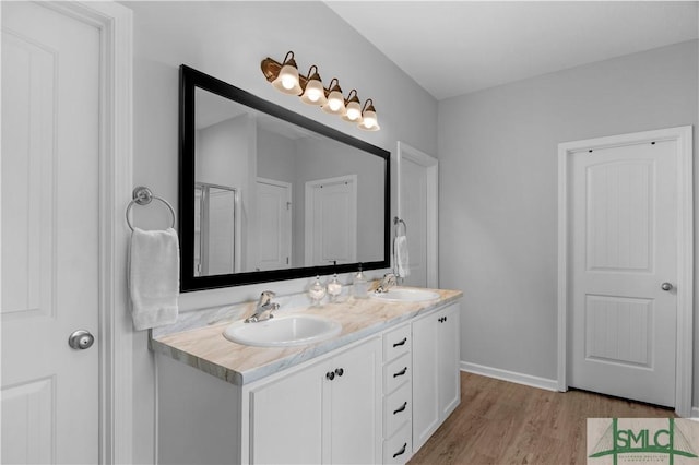 full bath featuring wood finished floors, double vanity, and baseboards