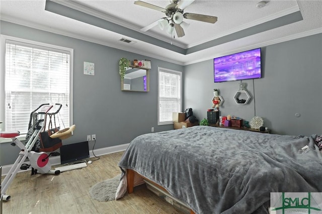 bedroom featuring a tray ceiling, crown molding, wood finished floors, baseboards, and ceiling fan