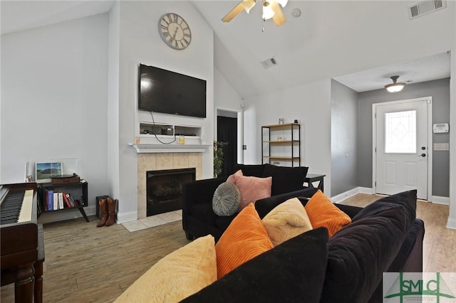 living area with wood finished floors, high vaulted ceiling, a ceiling fan, a tiled fireplace, and baseboards