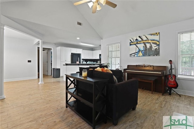 living area with decorative columns, ceiling fan, light wood finished floors, baseboards, and high vaulted ceiling