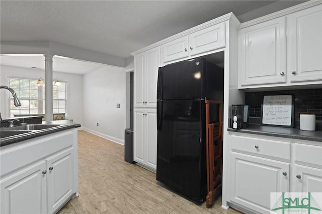 kitchen with freestanding refrigerator, dark countertops, a sink, and white cabinetry