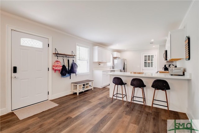 kitchen featuring white fridge with ice dispenser, white cabinetry, dark wood-style flooring, a peninsula, and ornamental molding