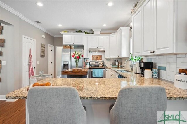 186 Goodman Dr, Midway, GA 31320 - kitchen with stainless steel appliances, under cabinet range hood, a sink, light stone counters, and a breakfast bar