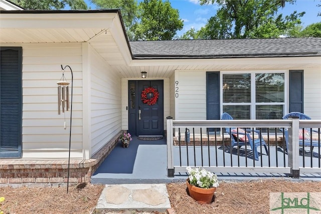 doorway to property featuring roof with shingles and covered porch