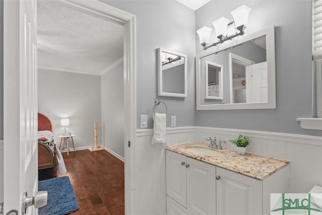 bathroom featuring wood finished floors, crown molding, a wainscoted wall, vanity, and a textured ceiling