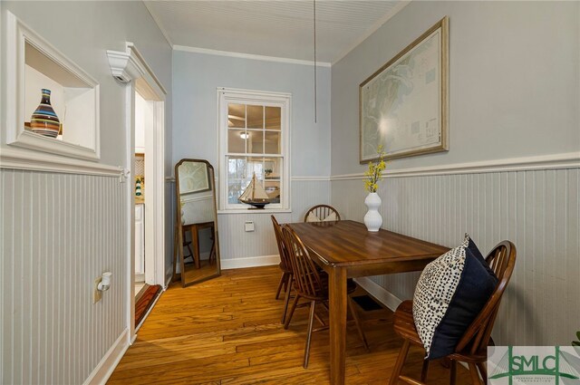 dining space featuring wood finished floors, a wainscoted wall, and crown molding