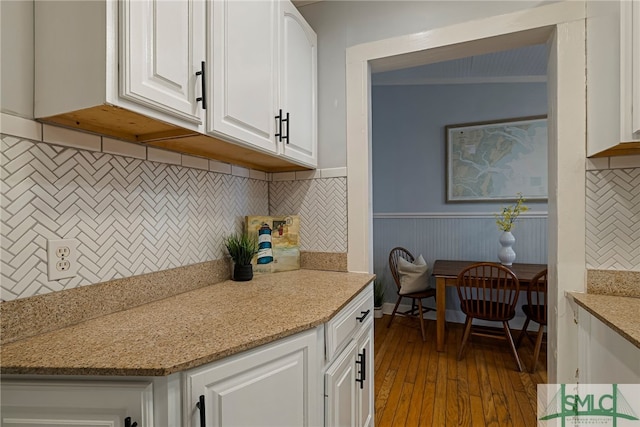 kitchen featuring white cabinetry, wood finished floors, backsplash, light stone counters, and wainscoting