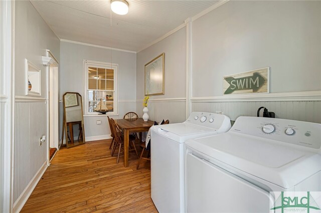 laundry room with ornamental molding, washing machine and dryer, light wood-type flooring, and a wainscoted wall