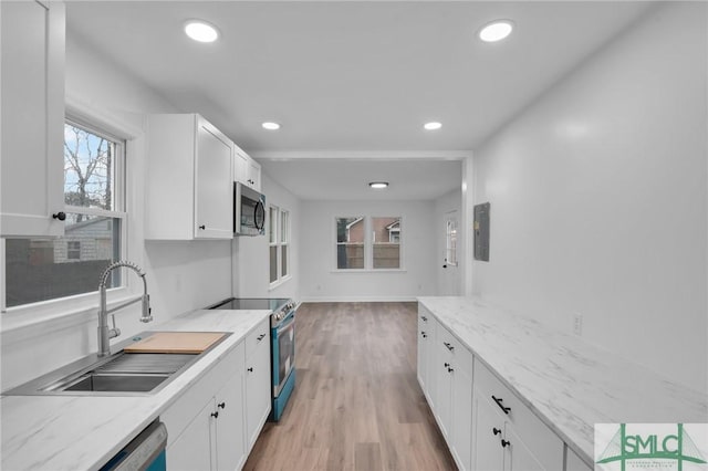 kitchen with appliances with stainless steel finishes, a sink, white cabinetry, light wood finished floors, and recessed lighting