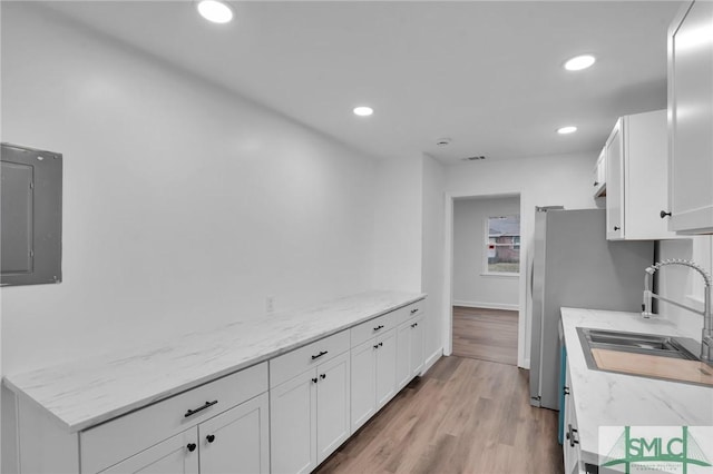 kitchen with a sink, electric panel, white cabinets, recessed lighting, and light wood-style floors