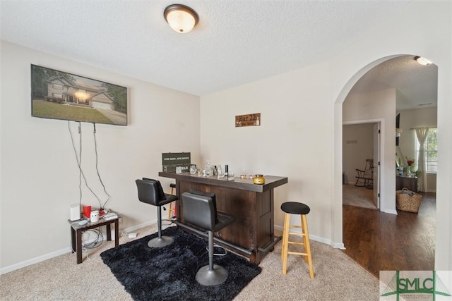 carpeted office space with arched walkways, a bar, a textured ceiling, and baseboards