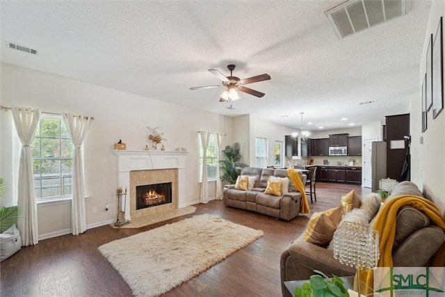 living room with plenty of natural light, a ceiling fan, dark wood-style flooring, a fireplace, and a textured ceiling