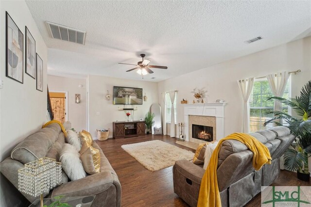 living area with a ceiling fan, wood finished floors, a textured ceiling, and a tiled fireplace