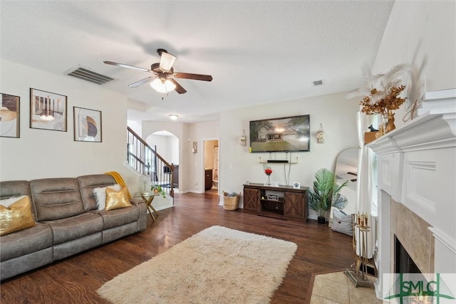 living room with a premium fireplace, arched walkways, a ceiling fan, wood finished floors, and stairway