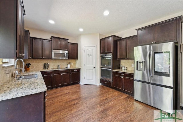 kitchen featuring appliances with stainless steel finishes, a sink, dark brown cabinets, dark wood finished floors, and backsplash