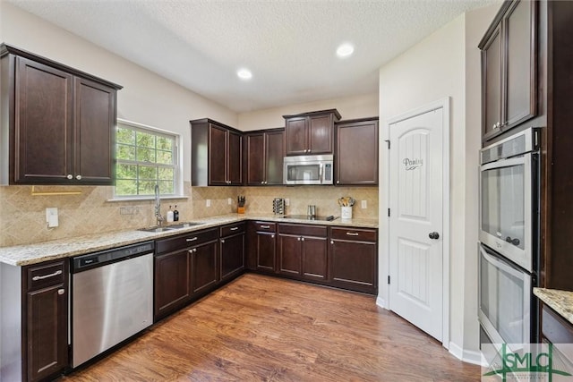 kitchen featuring appliances with stainless steel finishes, a sink, dark brown cabinetry, light wood finished floors, and light stone countertops