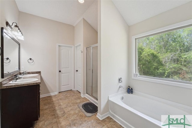 bathroom featuring a bath, a stall shower, double vanity, baseboards, and lofted ceiling