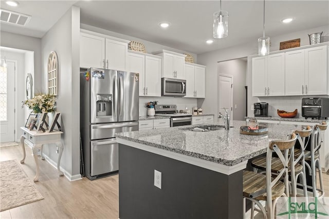 kitchen with appliances with stainless steel finishes, a sink, white cabinetry, an island with sink, and light wood-type flooring