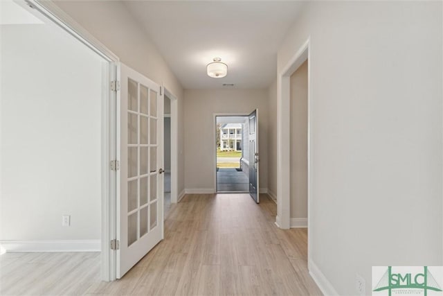 hallway with french doors, light wood-type flooring, and baseboards