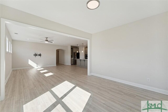 unfurnished living room featuring arched walkways, light wood-style flooring, and baseboards