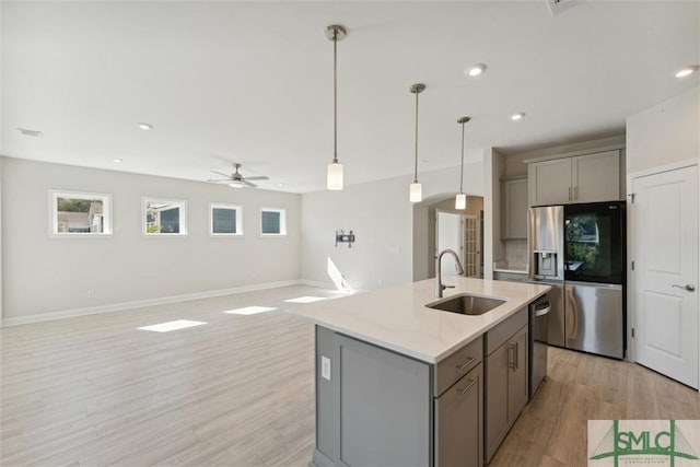 kitchen featuring a sink, gray cabinetry, appliances with stainless steel finishes, arched walkways, and light wood-type flooring
