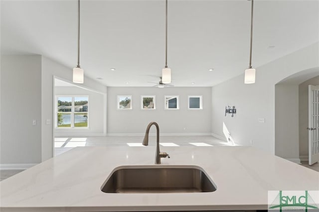 kitchen featuring a sink, open floor plan, arched walkways, ceiling fan, and pendant lighting