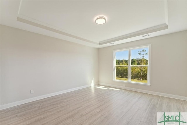 unfurnished room with a raised ceiling, light wood finished floors, and baseboards