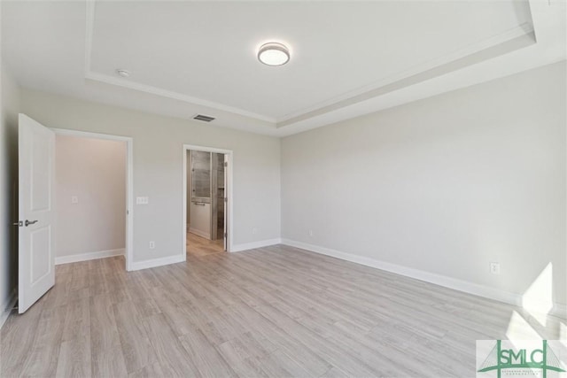 unfurnished bedroom featuring a tray ceiling, light wood finished floors, and baseboards