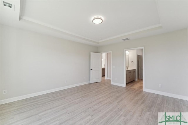 unfurnished bedroom with a raised ceiling, light wood-type flooring, baseboards, and connected bathroom