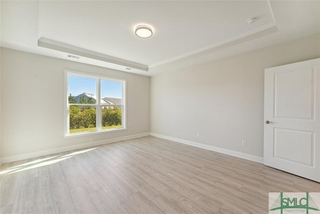 spare room with a tray ceiling and light wood-style floors