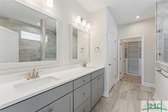bathroom with a tile shower, double vanity, marble look tiles, a spacious closet, and recessed lighting