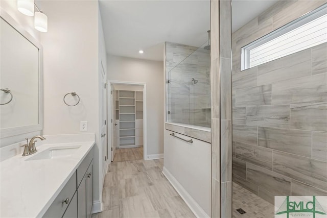 bathroom with tiled shower, vanity, a spacious closet, baseboards, and recessed lighting