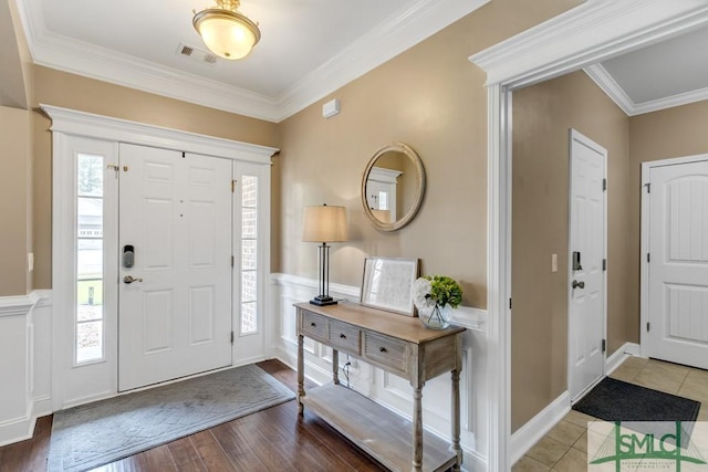 foyer with crown molding, a wainscoted wall, healthy amount of natural light, wood finished floors, and a decorative wall