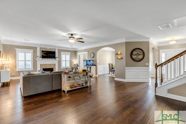 living area with arched walkways, ceiling fan, hardwood / wood-style flooring, a fireplace, and crown molding