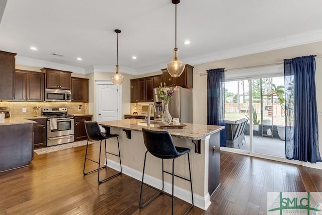 kitchen with appliances with stainless steel finishes, dark wood-type flooring, backsplash, light stone countertops, and dark brown cabinets