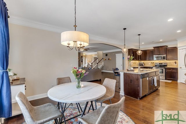 dining space with arched walkways, baseboards, wood finished floors, a chandelier, and ornamental molding