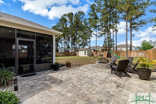 view of patio featuring a sunroom, a storage shed, an outdoor fire pit, a playground, and an outdoor structure