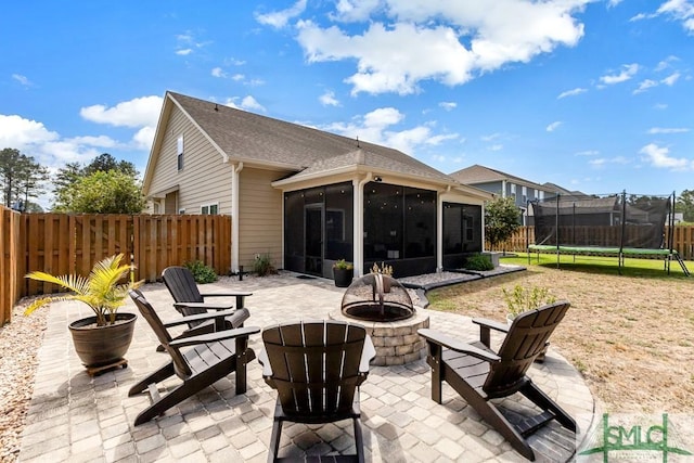 view of patio / terrace with a fire pit, a trampoline, a sunroom, and a fenced backyard