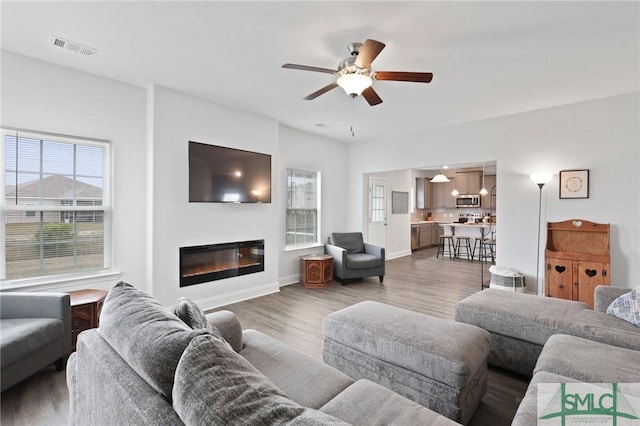 living area with light wood-style floors, ceiling fan, a glass covered fireplace, and baseboards