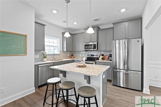 kitchen featuring appliances with stainless steel finishes, gray cabinetry, a sink, wood finished floors, and recessed lighting