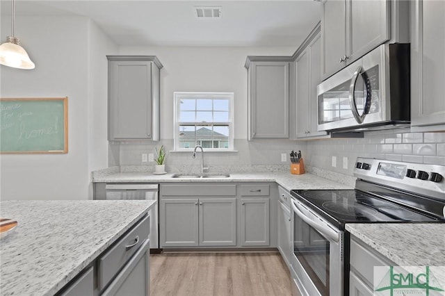 kitchen featuring appliances with stainless steel finishes, a sink, gray cabinets, and light wood-type flooring