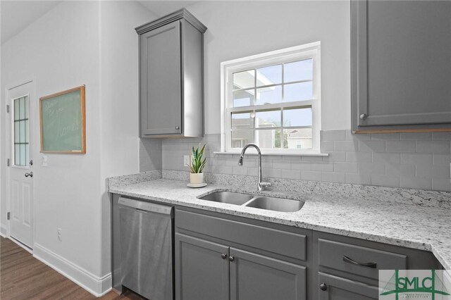 kitchen with gray cabinetry, stainless steel dishwasher, a sink, dark wood-style floors, and tasteful backsplash