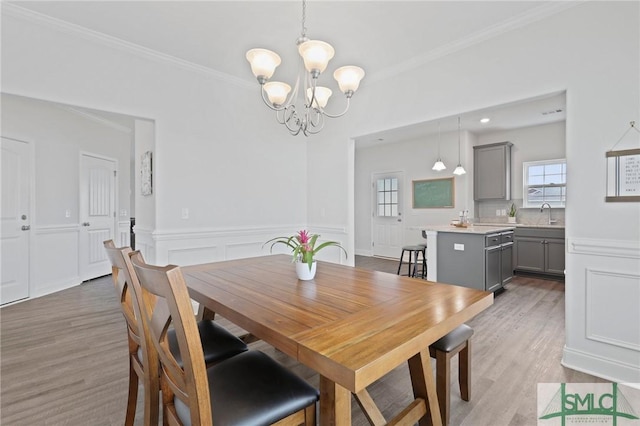 dining room with a chandelier, ornamental molding, healthy amount of natural light, light wood-style floors, and a wainscoted wall