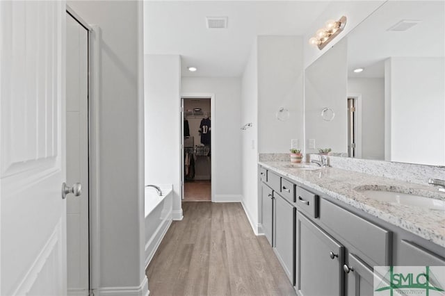 bathroom with wood finished floors, a walk in closet, a garden tub, double vanity, and baseboards