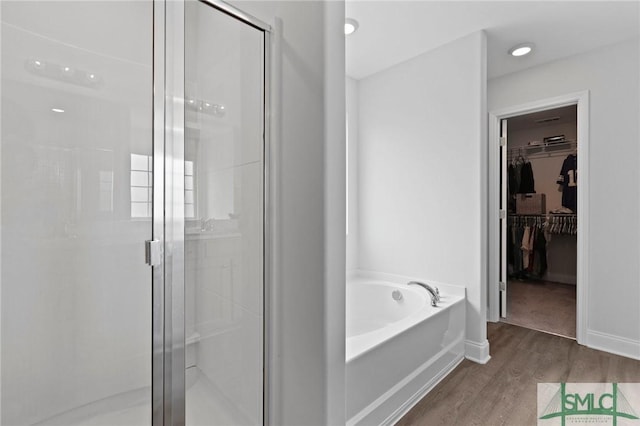 full bathroom with a stall shower, a walk in closet, wood finished floors, and a bath